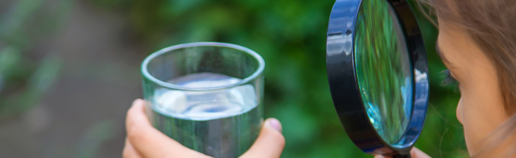 Ein Mädchen schaut mit einer Lupe auf ein Glas Wasser.