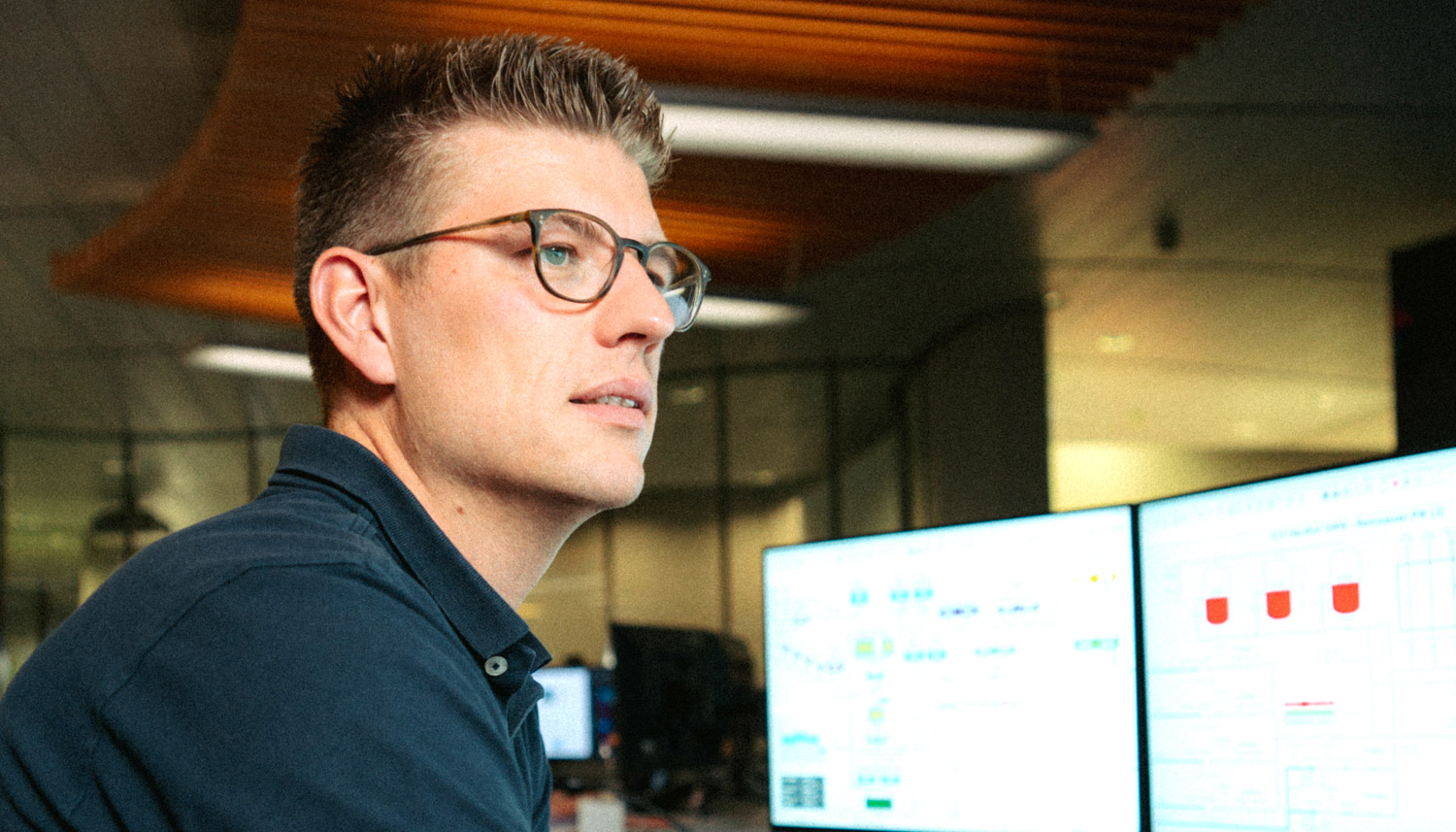 Automationsingenieur mit Brille sitzt vor mehreren Monitoren.