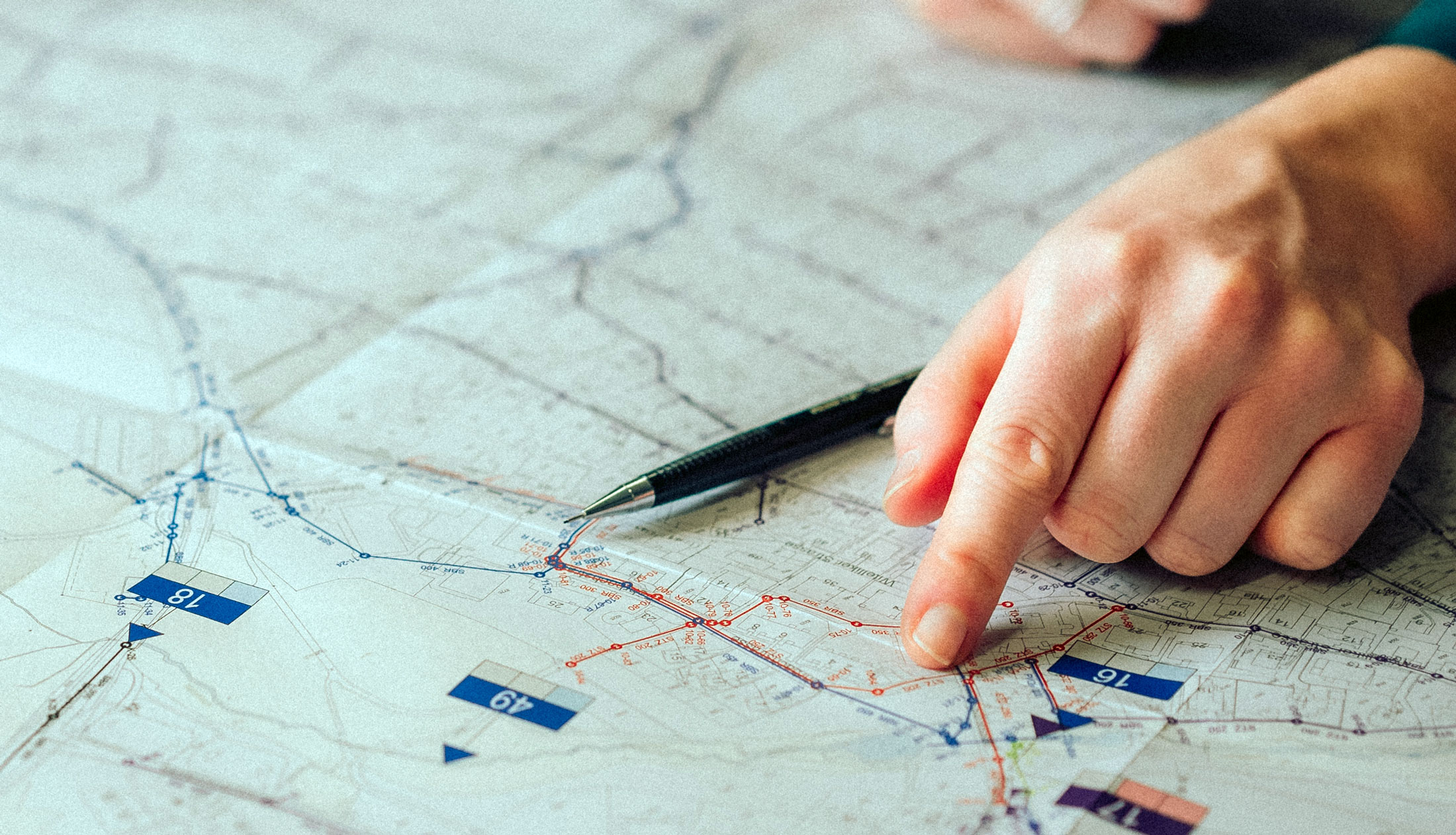 Nahaufnahme einer Hand, die auf einen detaillierten Stadtplan mit markierten Punkten zeigt und auf dem ein Stift liegt.