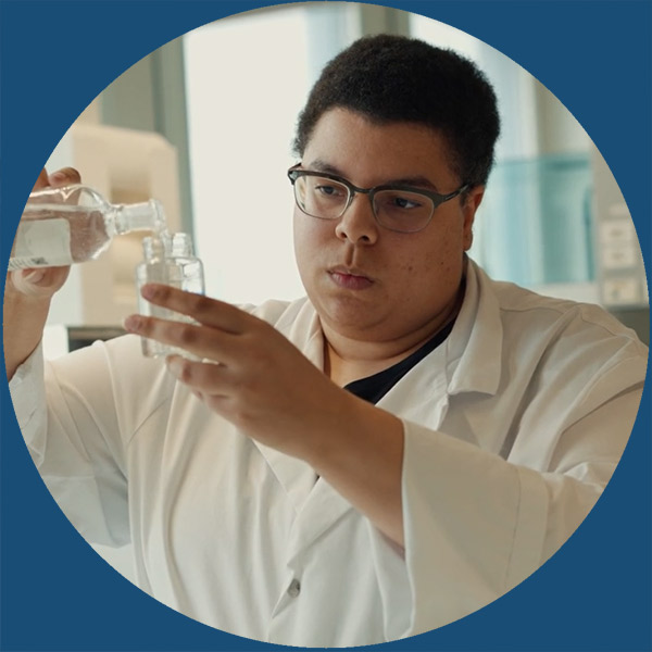 Eine Person in einem Laborkittel gießt in einer Laborumgebung Flüssigkeit von einer Flasche in eine andere.